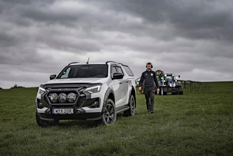 Vit Isuzu D-Max Double Cab med flakkåpa parkerad på lantlig åker – skördetröska i bakgrunden och lantbrukare går mot bilen.