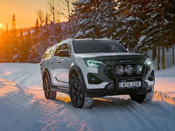 Isuzu pickup i djup snö med skogen bakom och vintersolen som lyser över landskapet – styrka i kyla.