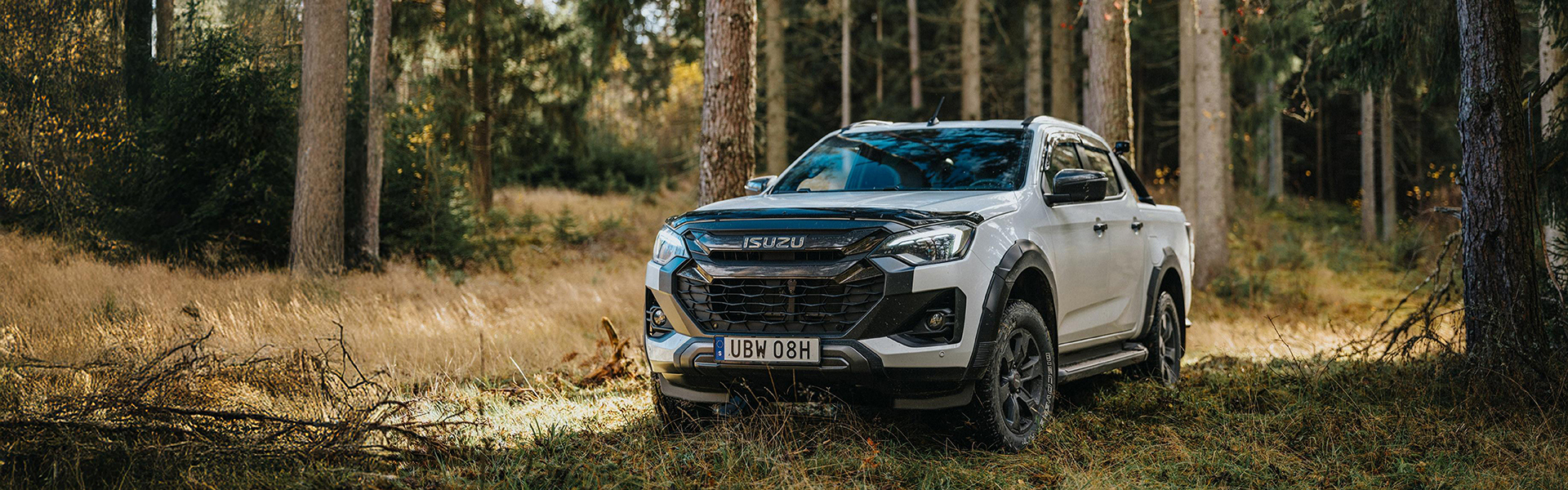 Isuzu pickup i grönskande skog med solstrålar som lyser genom trädens lövverk.