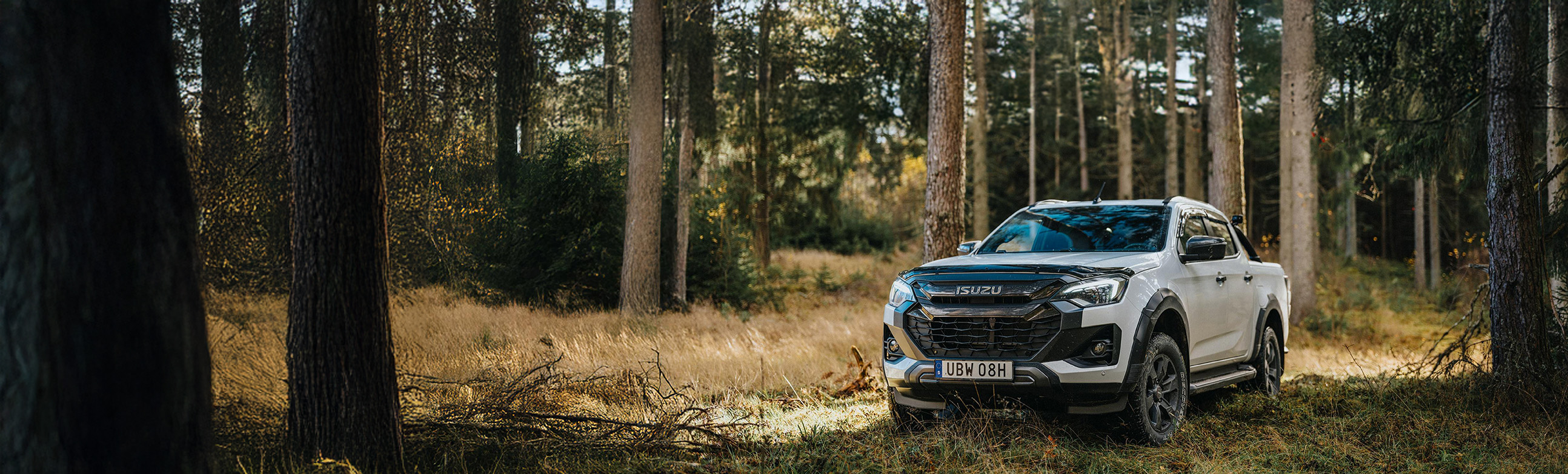 Isuzu pickup i grönskande skog med solstrålar som lyser genom trädens lövverk.